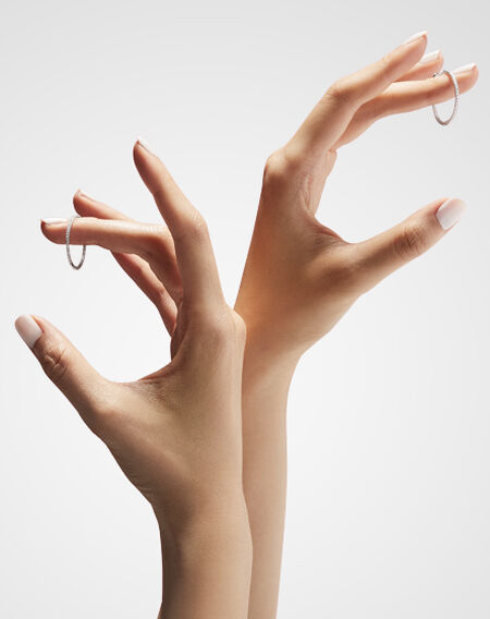 Mains de femmes tenant une paire de boucles d'oreilles en diamant Birks Essentiels.